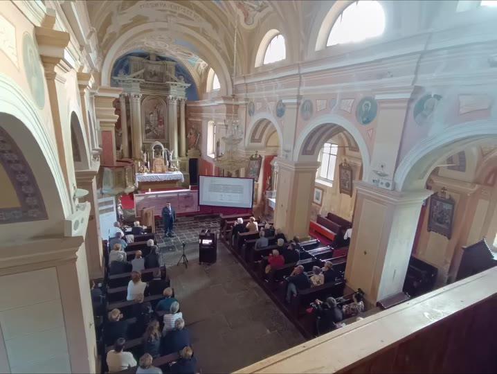 Interno della chiesa dei Santi Ermagora e Fortunato a Gerovo durante la conferenza, con il pubblico e lo schermo delle proiezioni