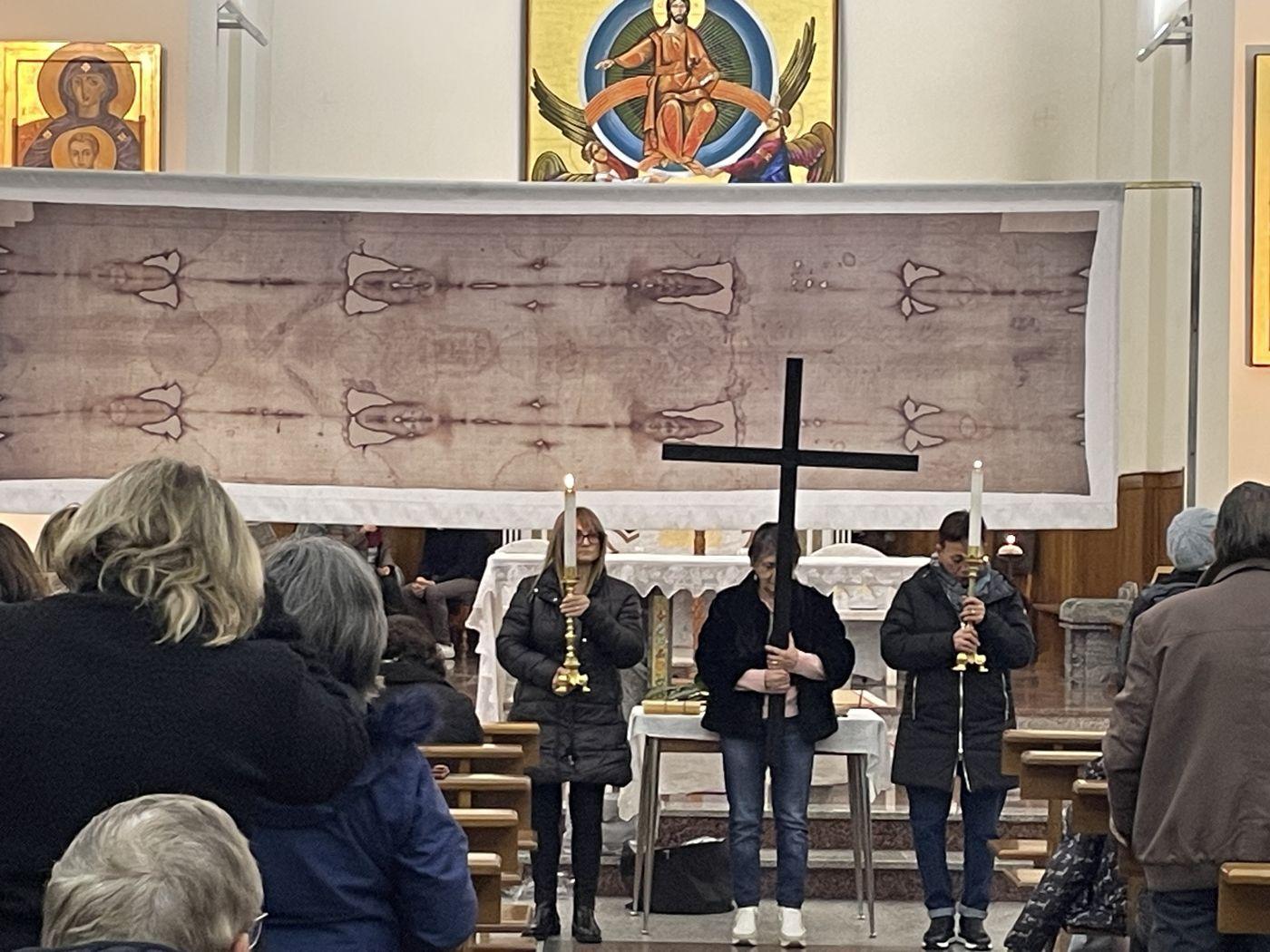Fedeli davanti alla copia della Sindone esposta sotto il mosaico dell'abside, con la croce e due ceri